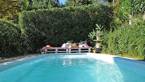 Ein Swimmingpool mit weißer Liegefläche und einer Sitzgruppe mit Kissen und einem Korb.