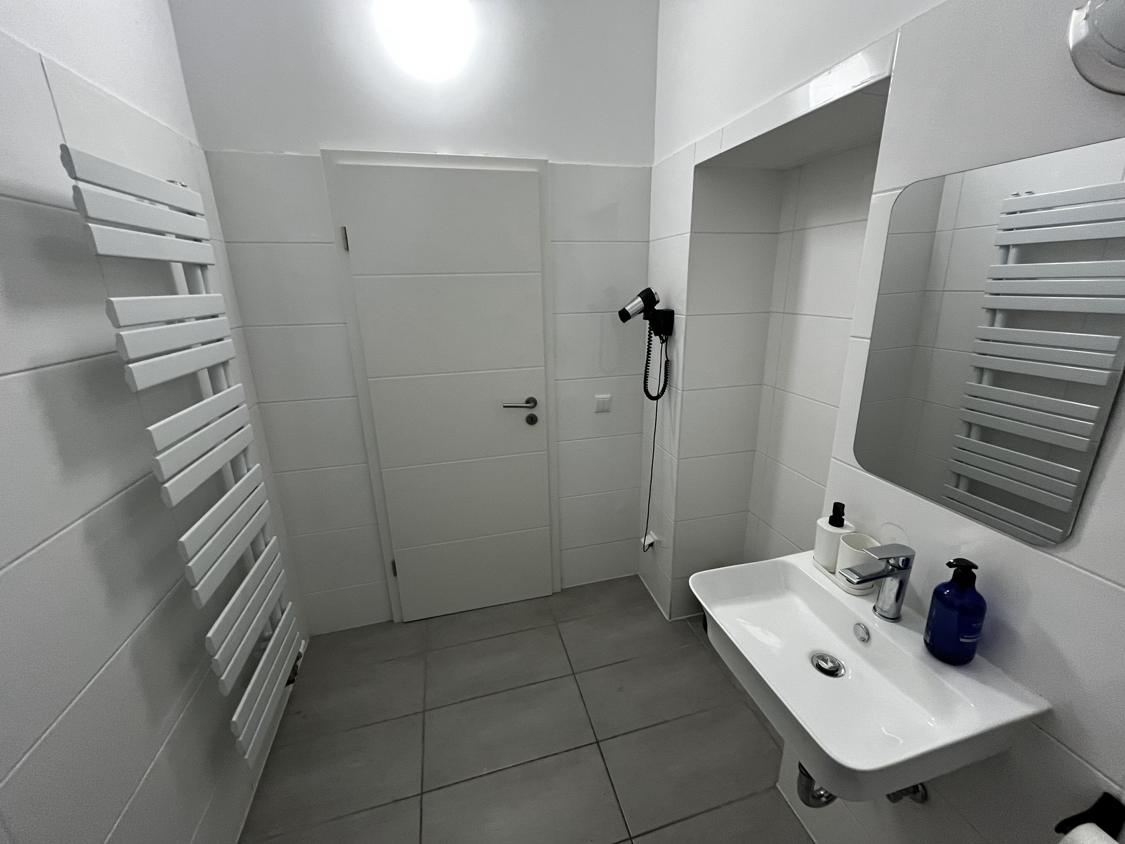 Ein Badezimmer mit weißem Waschbecken, einem Spiegel, einem Handtuchhalter und einer Duschbrause.