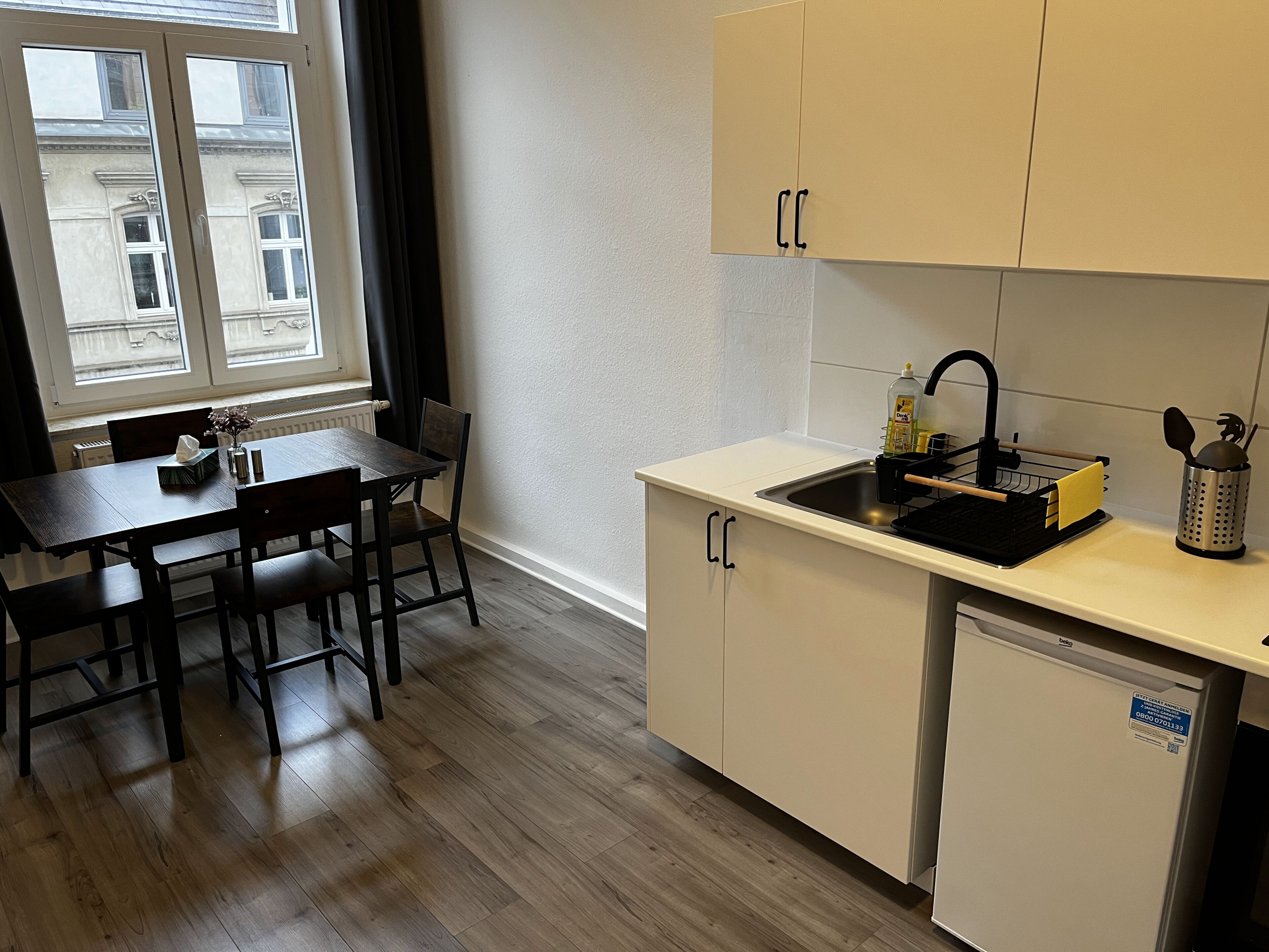 Eine kleine Küche mit Esstisch, Stühlen, Spüle und Kühlschrank.