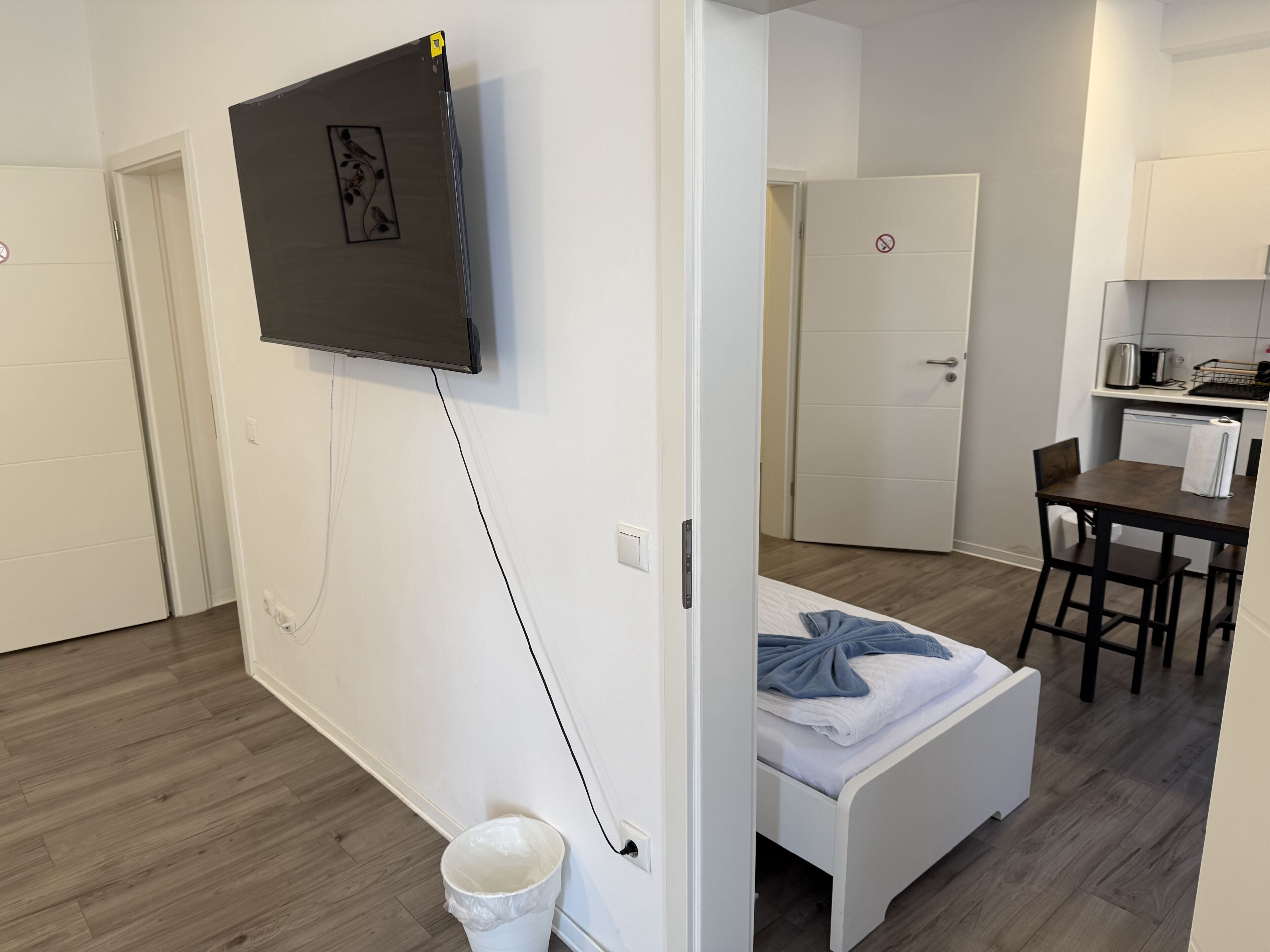 Habitació d'hotel moderna i compacte amb llit, taula petita, cadira, cuineta i televisió penjada a la paret.