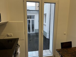 A kitchen with a built-in oven, a dining table, and a sliding glass door leading to an outdoor area with a wooden deck. - CityStay Bergisch Gladbach (Bergisch Gladbach)