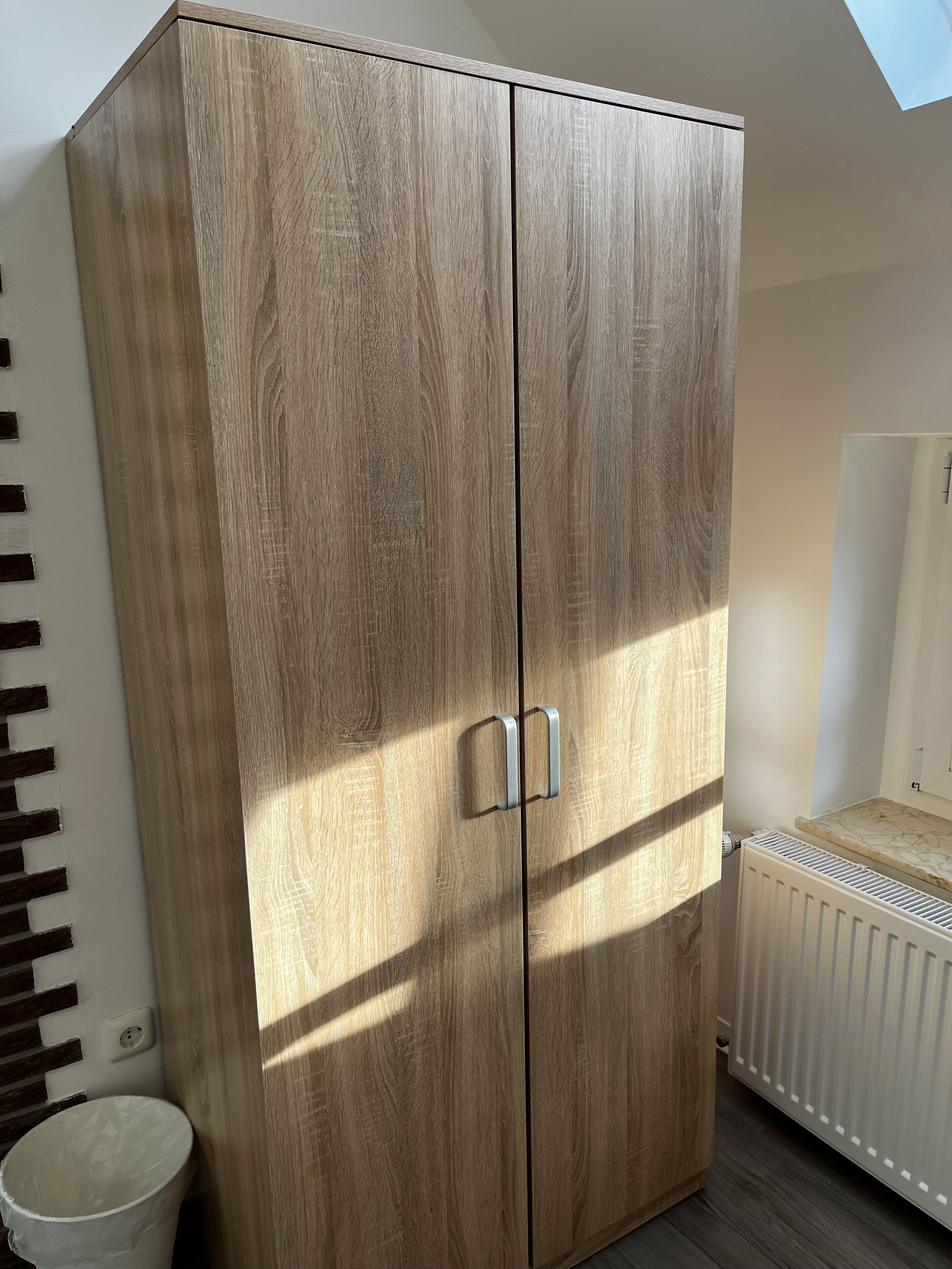 A wardrobe with a wooden finish, a radiator, and a white floor.