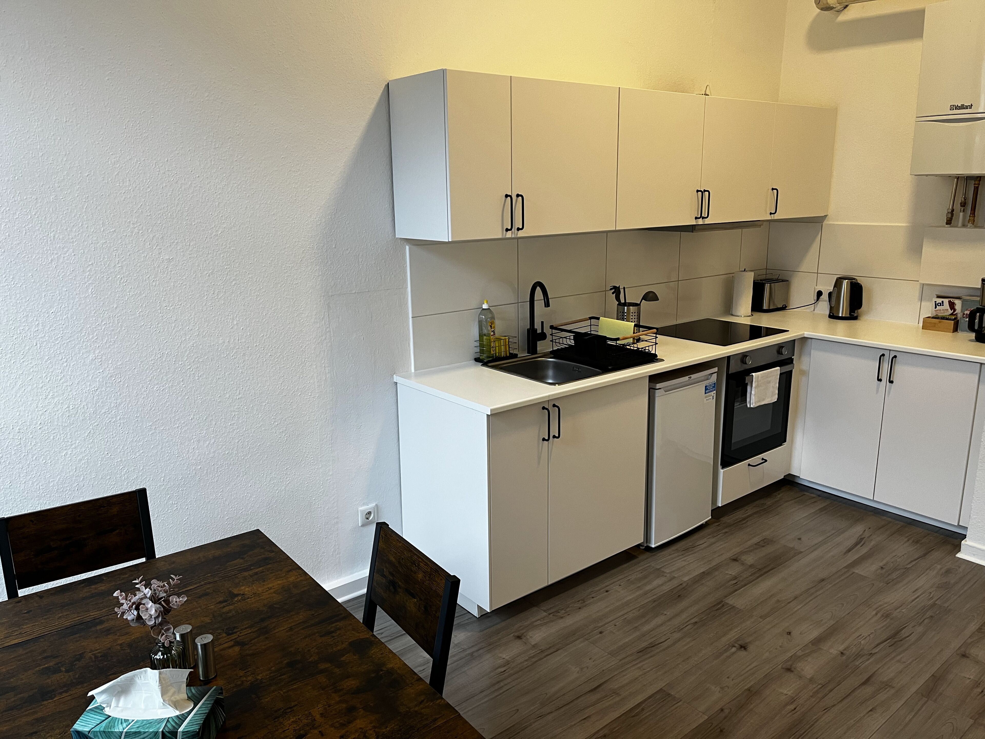 Une cuisine de taille réduite avec des meubles blancs, un évier, une cuisinière et un lave-vaisselle.