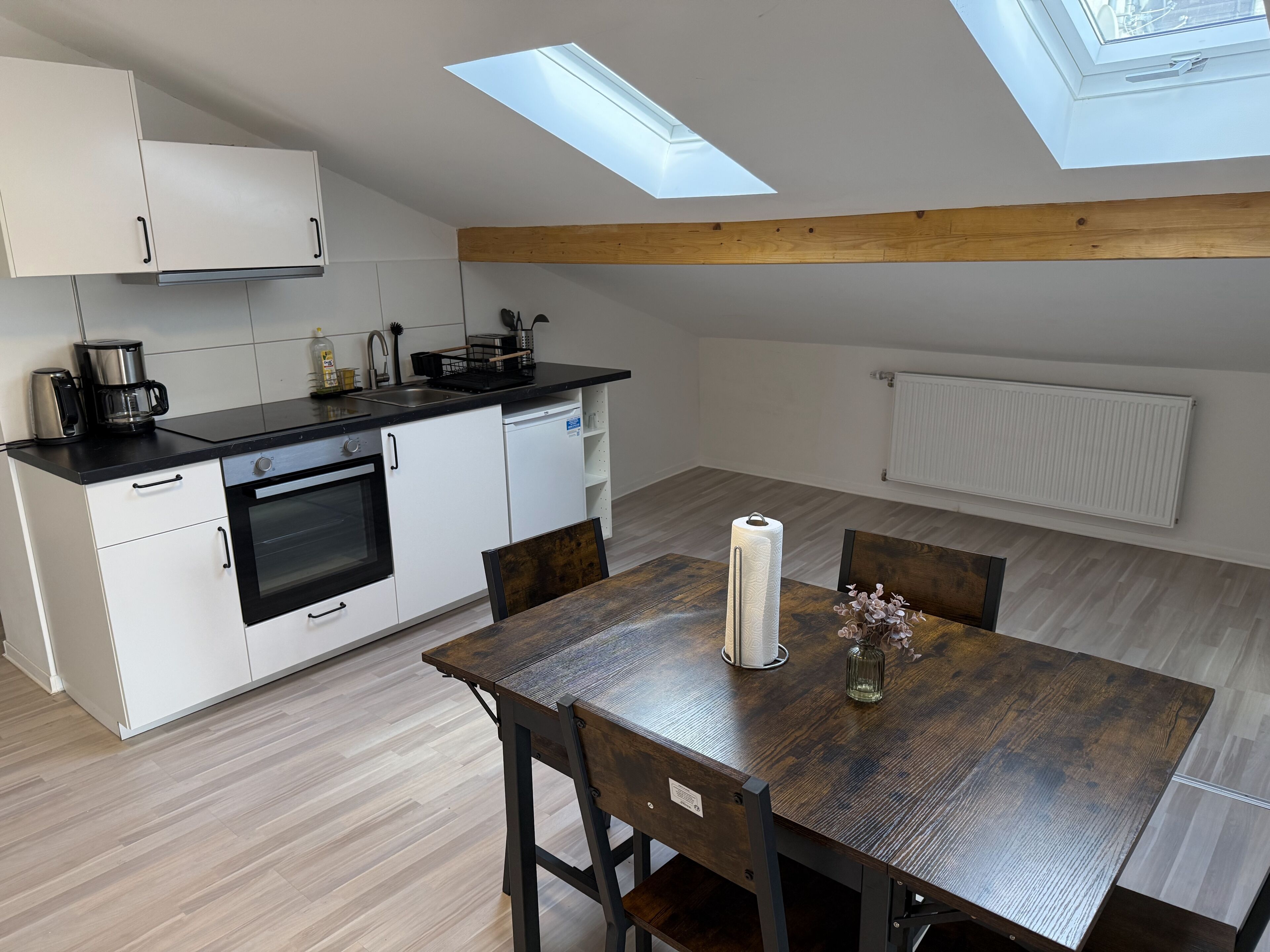 A modern kitchen with skylights, a dining table with chairs, and a radiator.