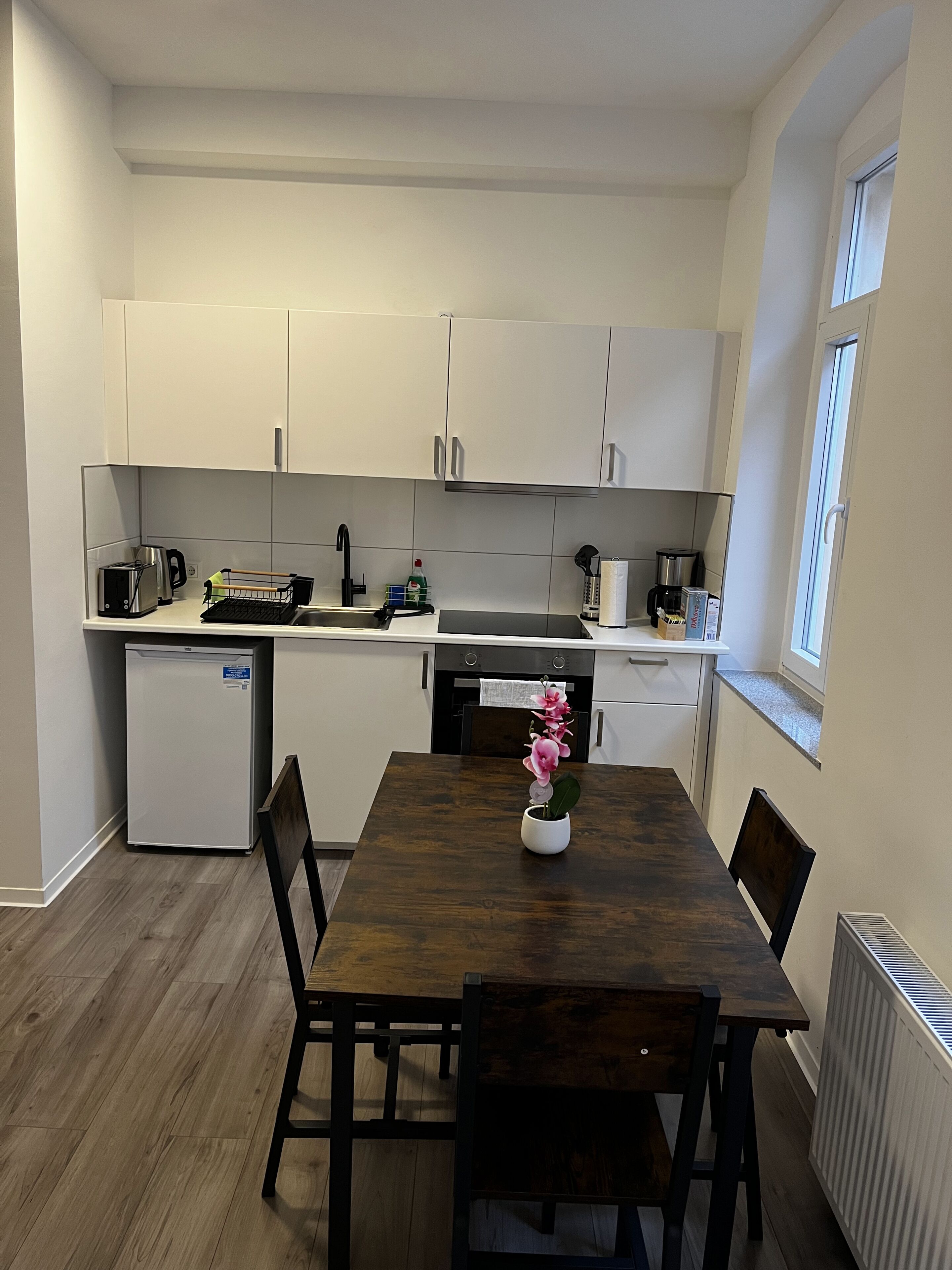 A compact kitchen with white cabinets, a small refrigerator, and a dining table with chairs.