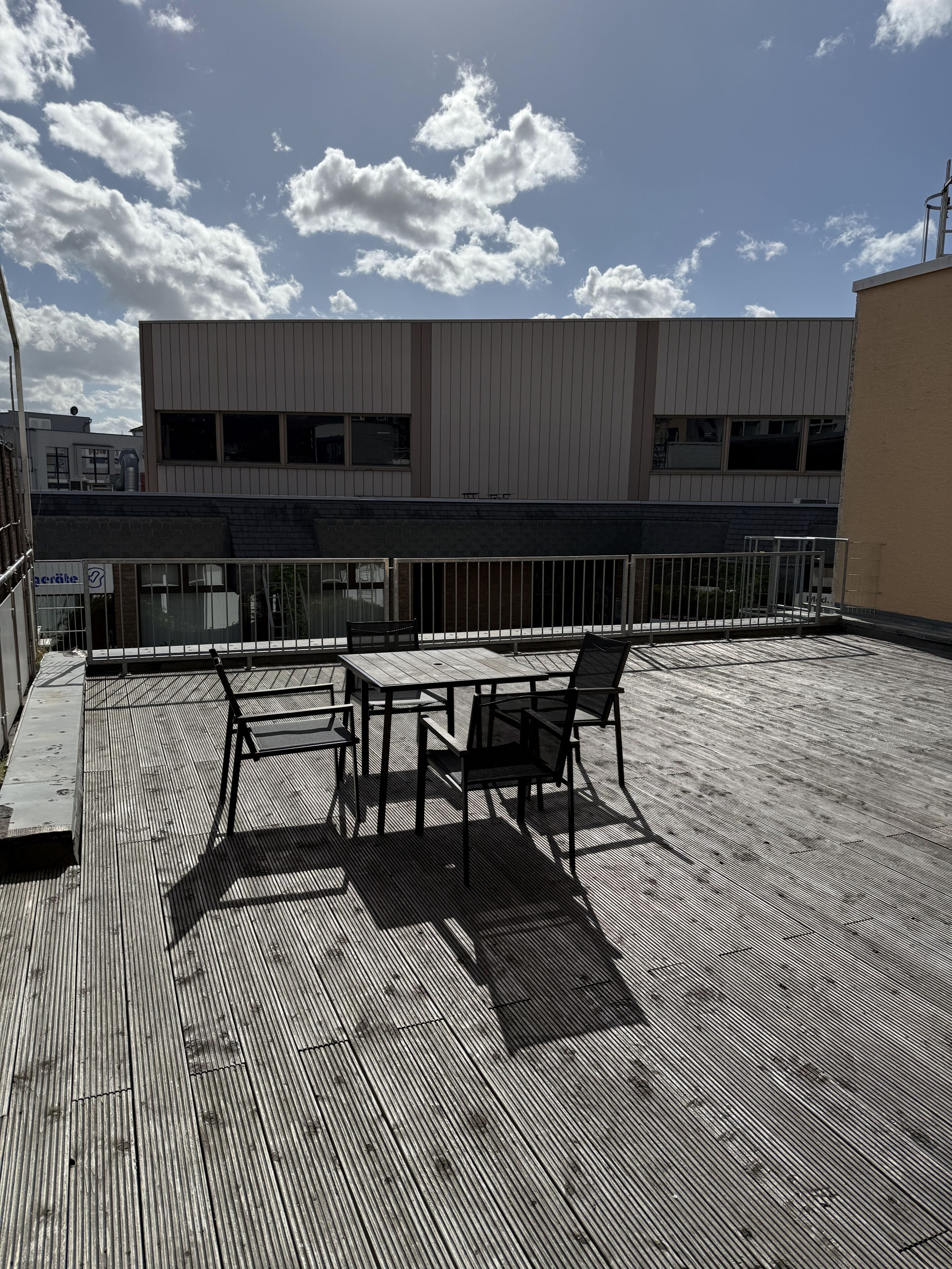 Une terrasse sur le toit, avec une table et des chaises, une rambarde et un bâtiment en arrière-plan.