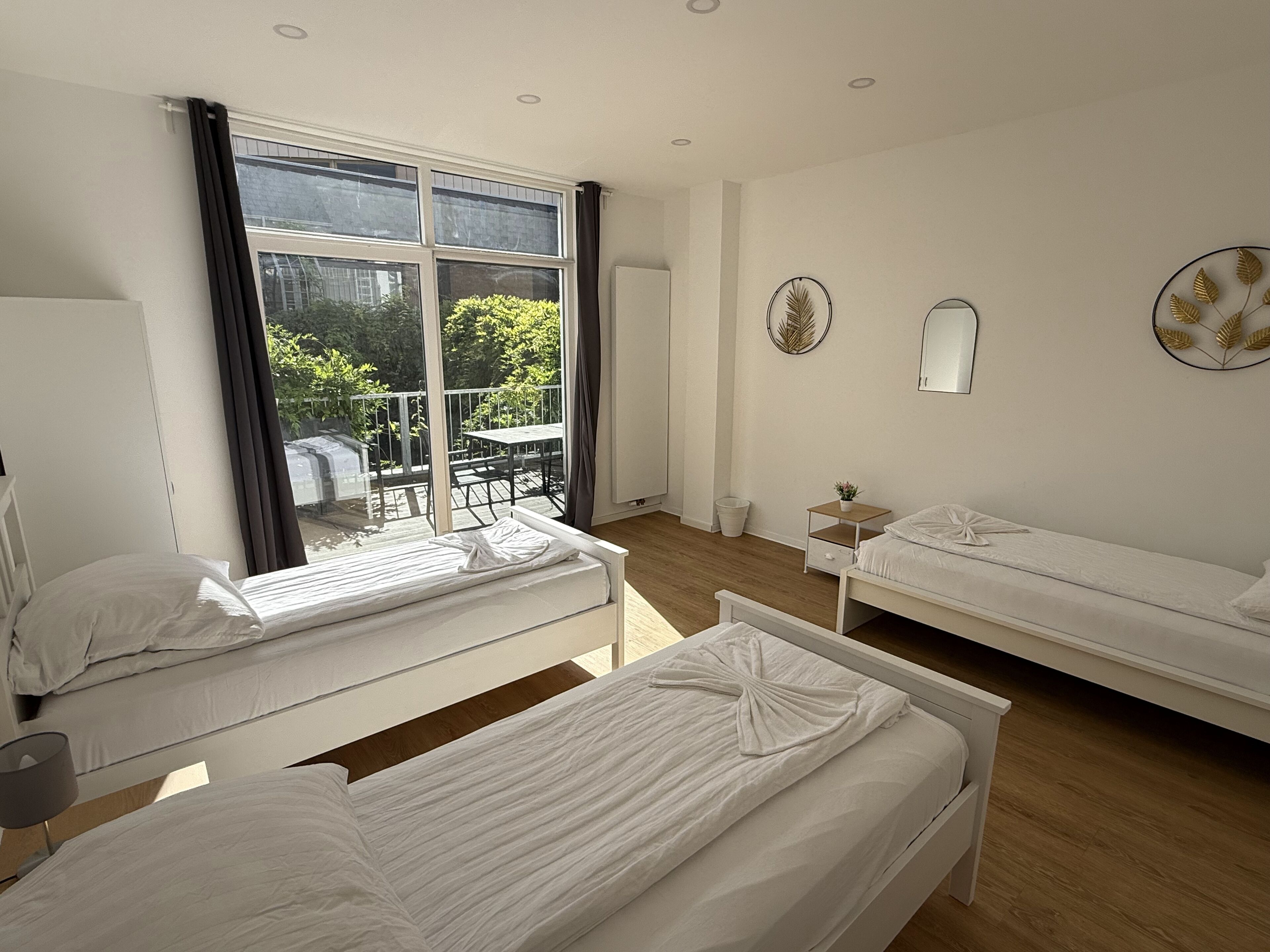 Ein Hotelzimmer mit zwei Betten, einem Fenster mit Vorhängen, einem kleinen Tisch und einem wandmontierten Spiegel.