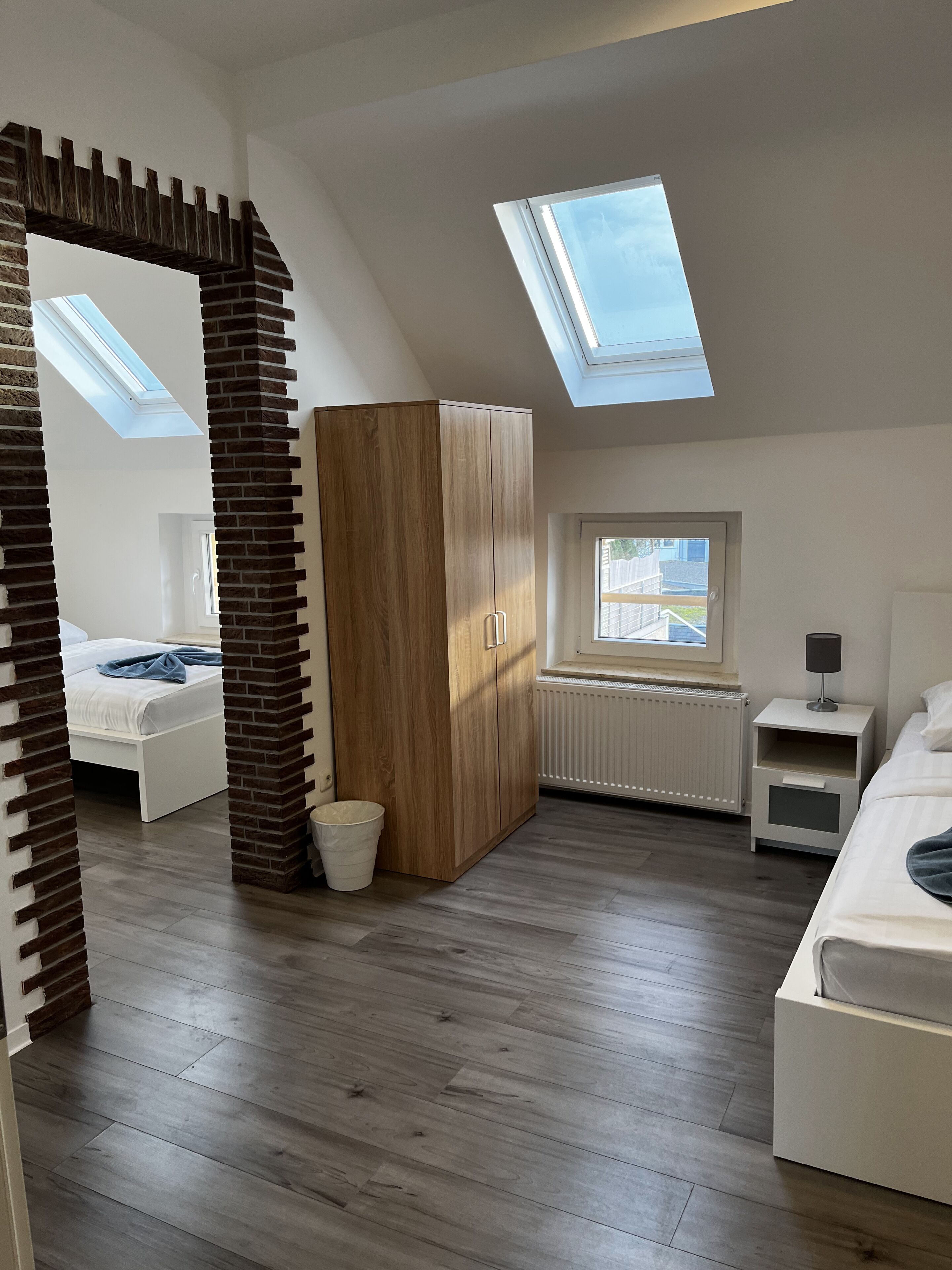 A modern bedroom with a skylight, a wooden wardrobe, a radiator, and a bedside table.