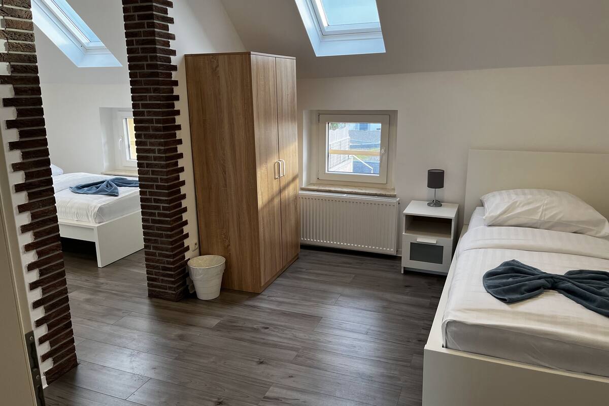 A bedroom with a skylight, a wardrobe, a radiator, a bedside table, and a bed.