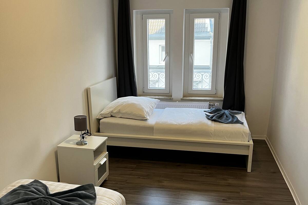 A bedroom with a bed, bedside table, lamp, and a window with curtains.
