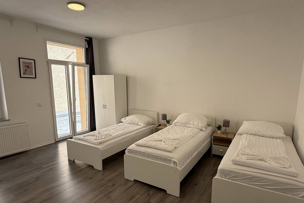 A room with two single beds, a wardrobe, a radiator, and a door leading to an outdoor area.