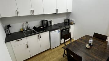 Une cuisine compacte avec des meubles blancs, un plan de travail noir, une machine à café, un grille-pain et un lave-vaisselle.