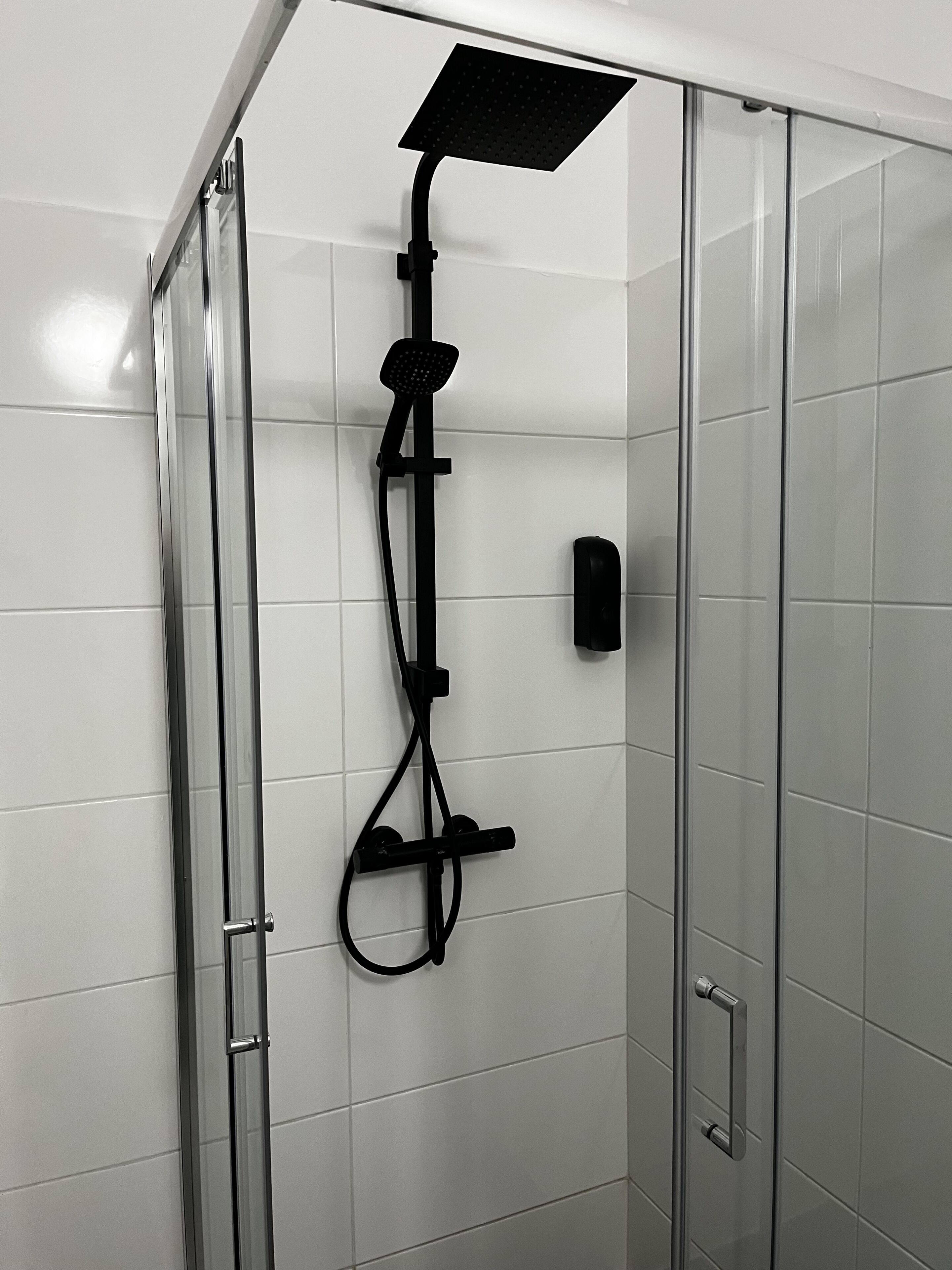 A glass-enclosed shower with a handheld showerhead and a fixed showerhead.