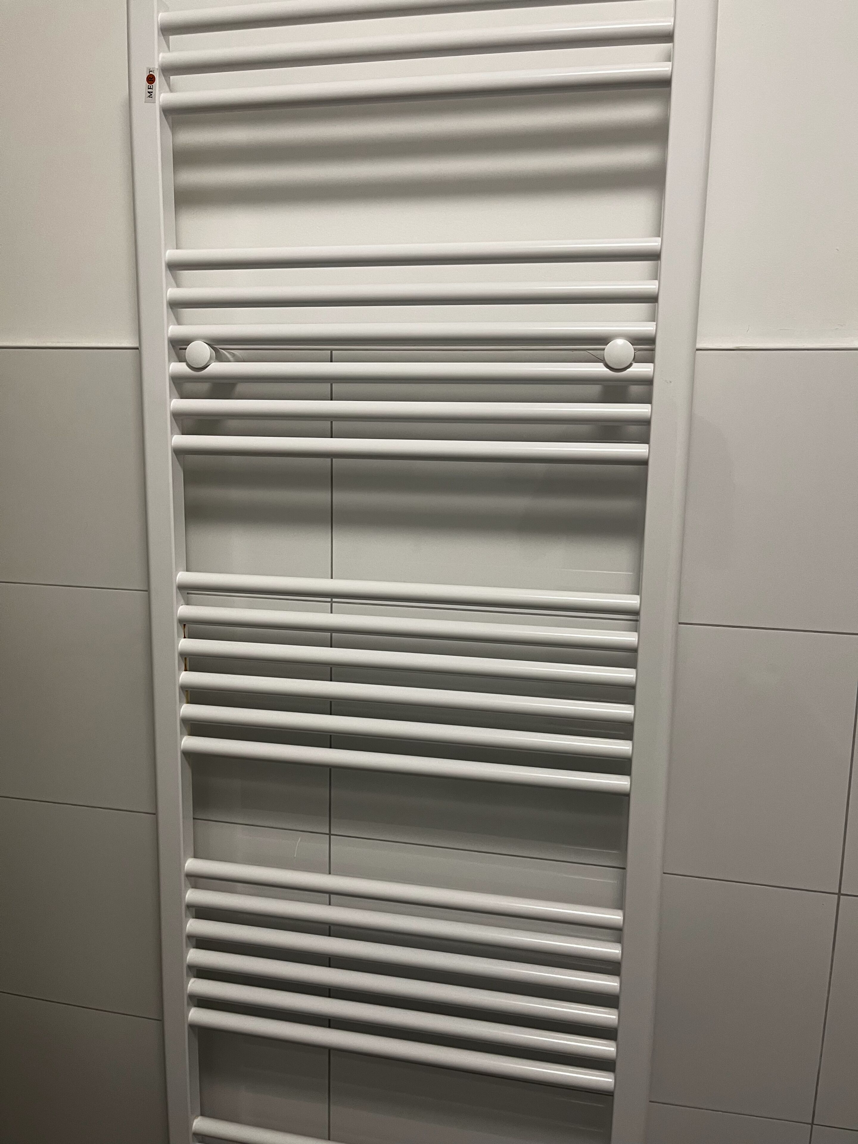 A white, wall-mounted radiator with horizontal slats and two round knobs.
