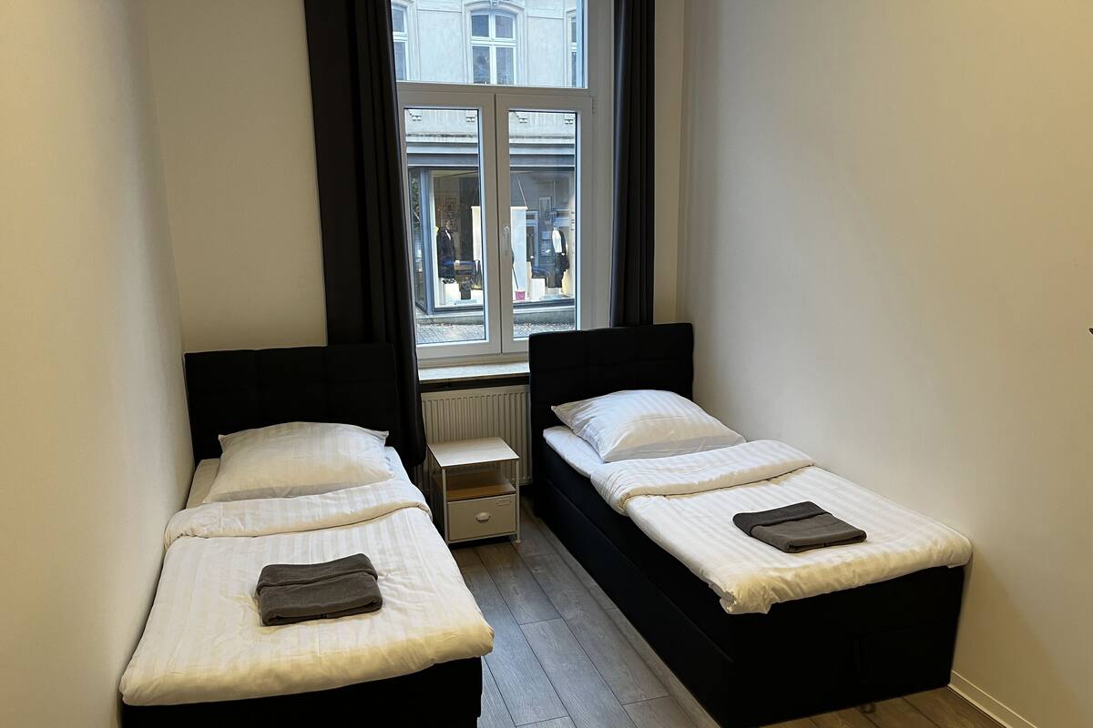 A small, clean room with two beds, a window, and a radiator.
