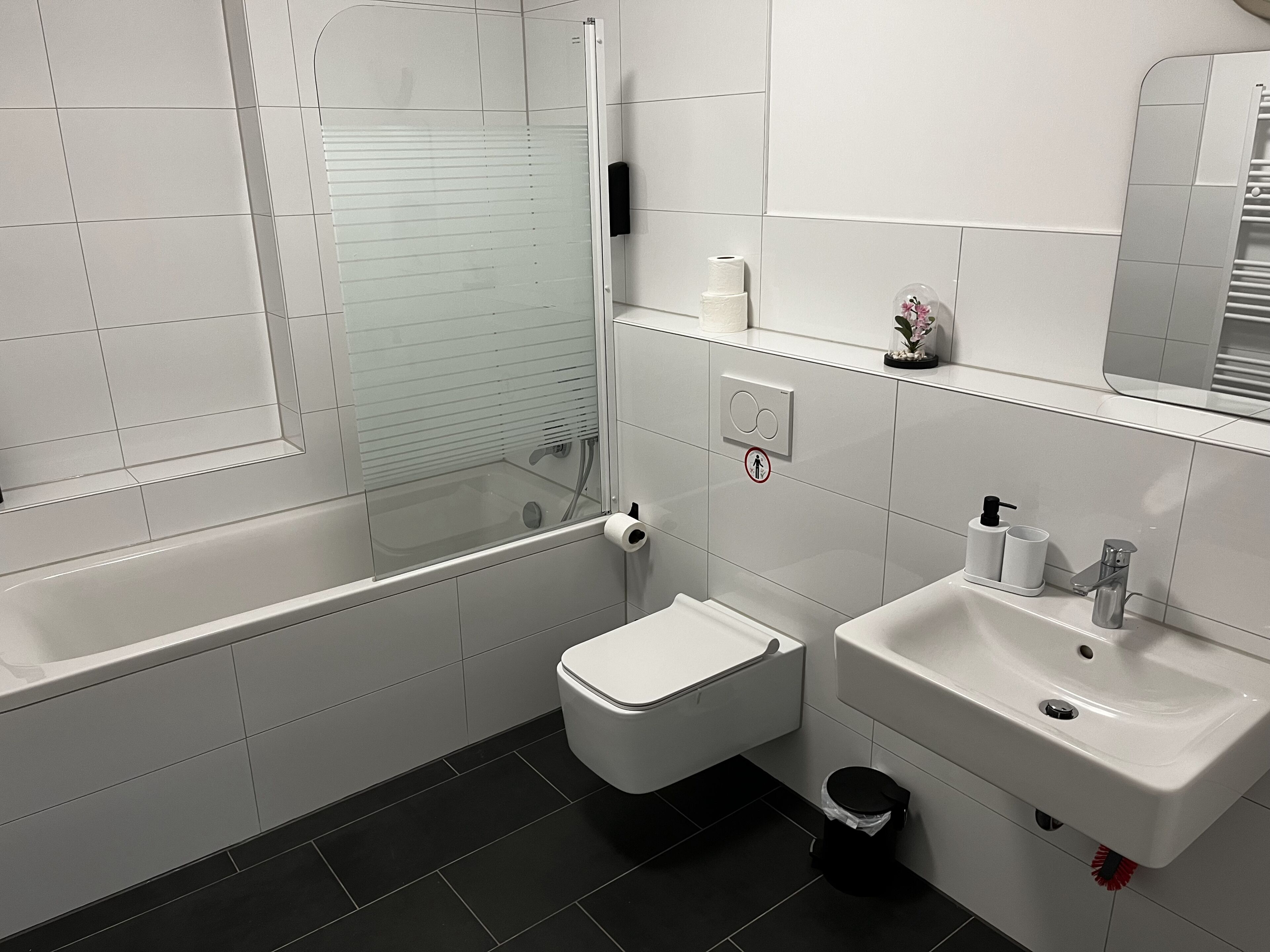 A modern bathroom with a glass-enclosed shower, a toilet, a sink, and a trash bin.