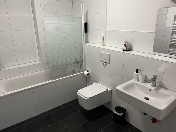 A modern bathroom with a glass-enclosed shower, a toilet, a sink, and a trash bin.