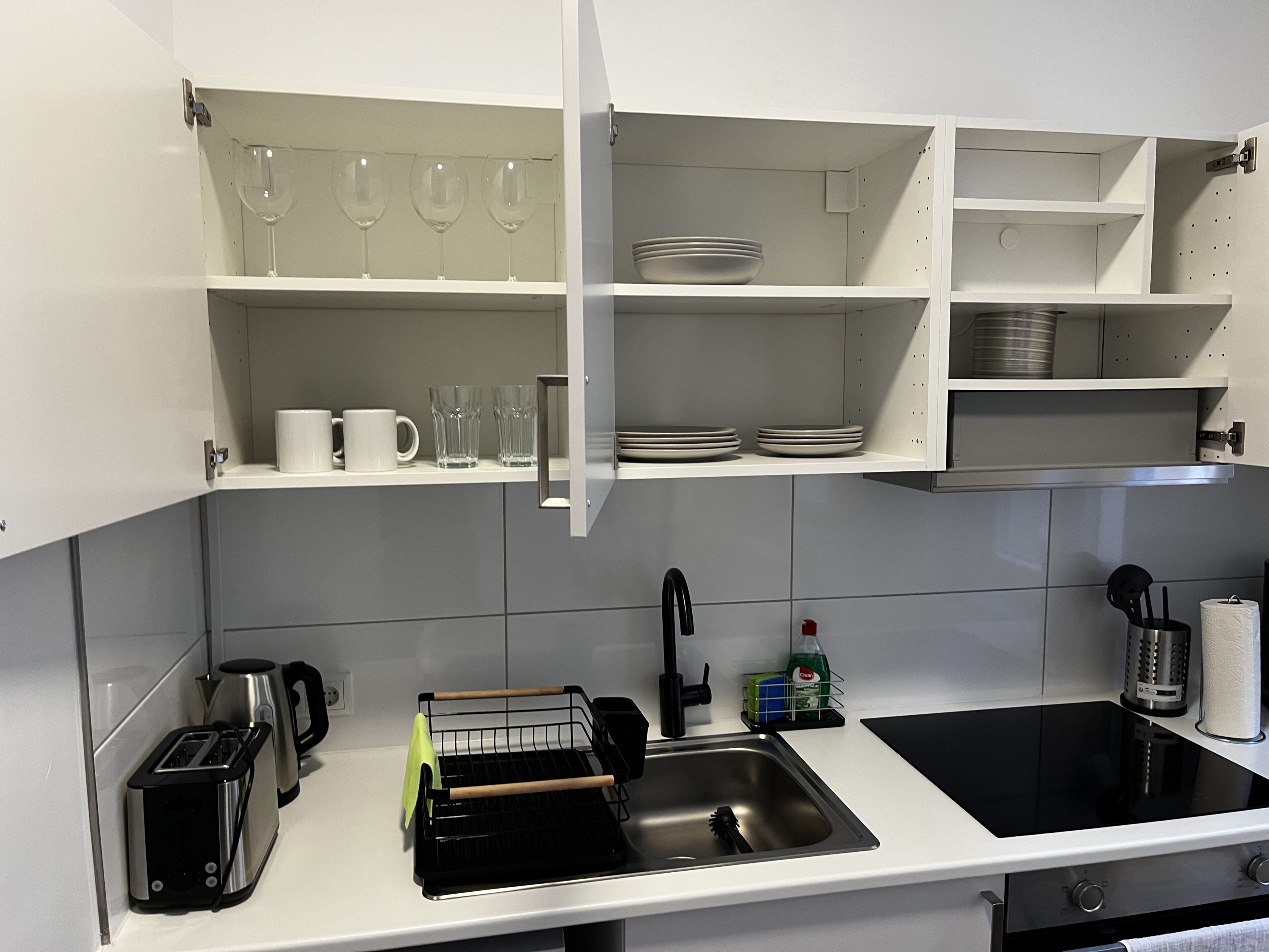A modern kitchen with white cabinets, a stainless steel sink, a black stove, and a coffee maker.