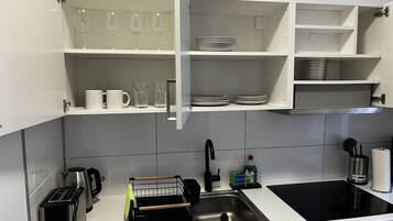 A modern kitchen with white cabinets, a stainless steel sink, a black stove, and a coffee maker.