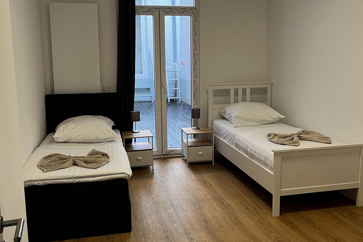 A bedroom with two beds, a window, and a door leading to an outdoor area.