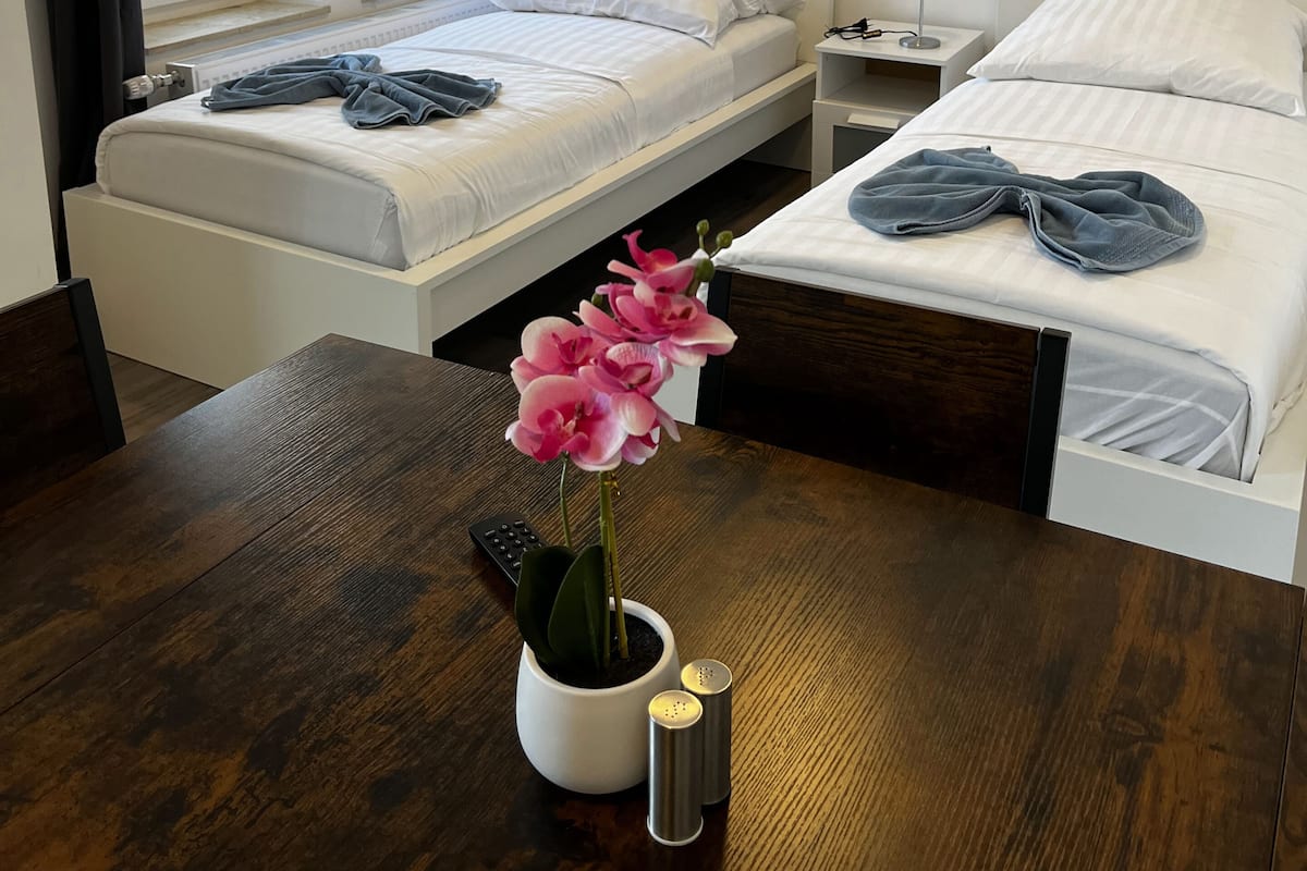 A hotel room with two beds, a wooden table, a potted plant, and a nightstand with a lamp.