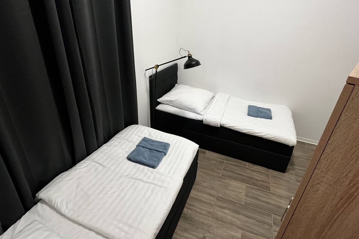 A small, single-bed room with a black headboard, a bedside lamp, and a wooden floor.