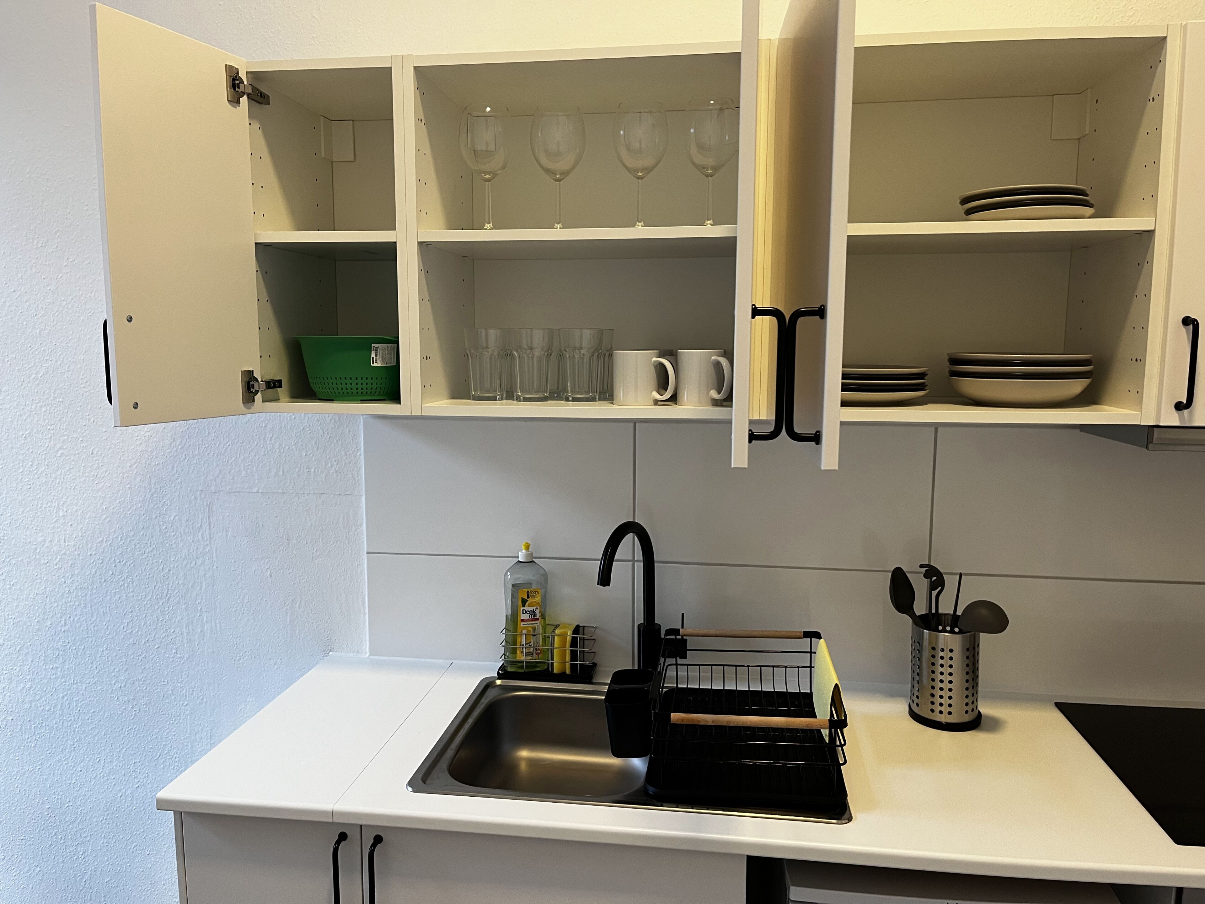 Una cocina con armarios blancos, un lavamanos y diversos utensilios.