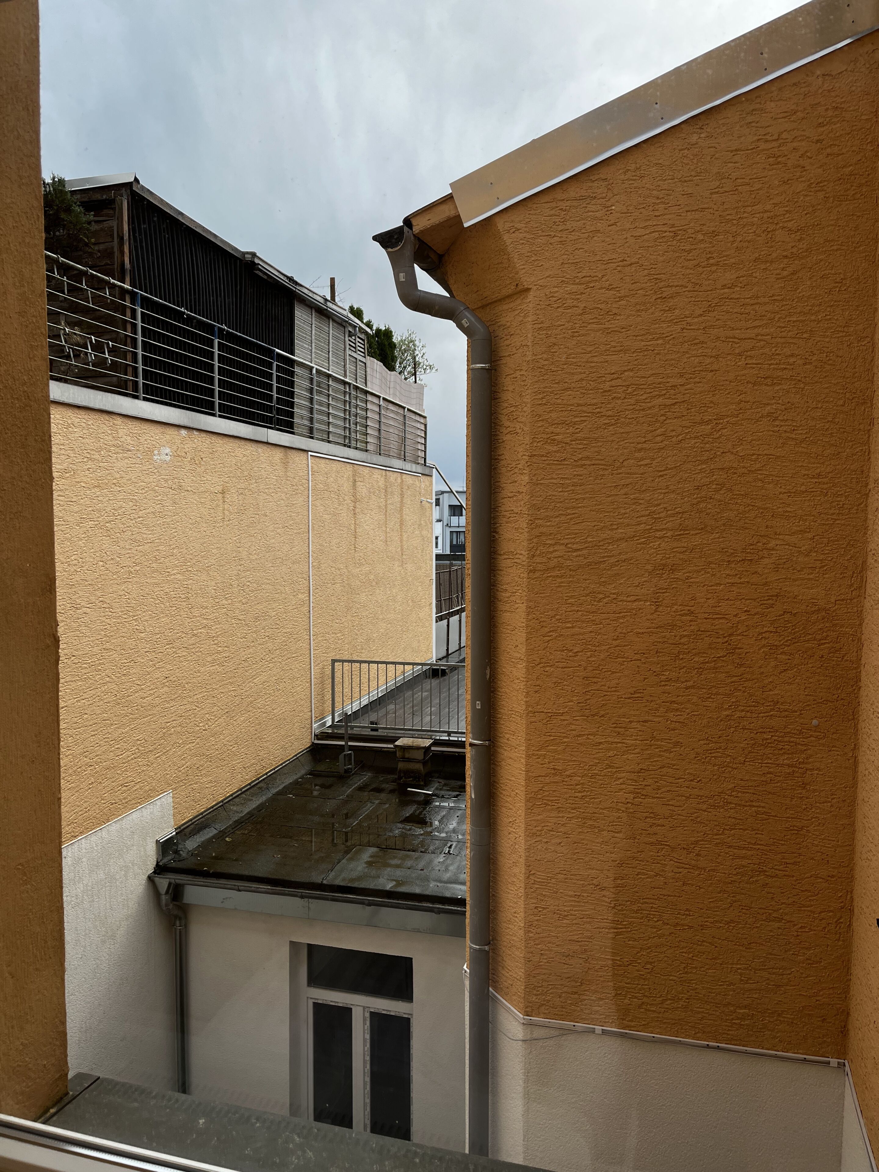 A multi-level building with a metal railing, a small window, and a visible pipe.