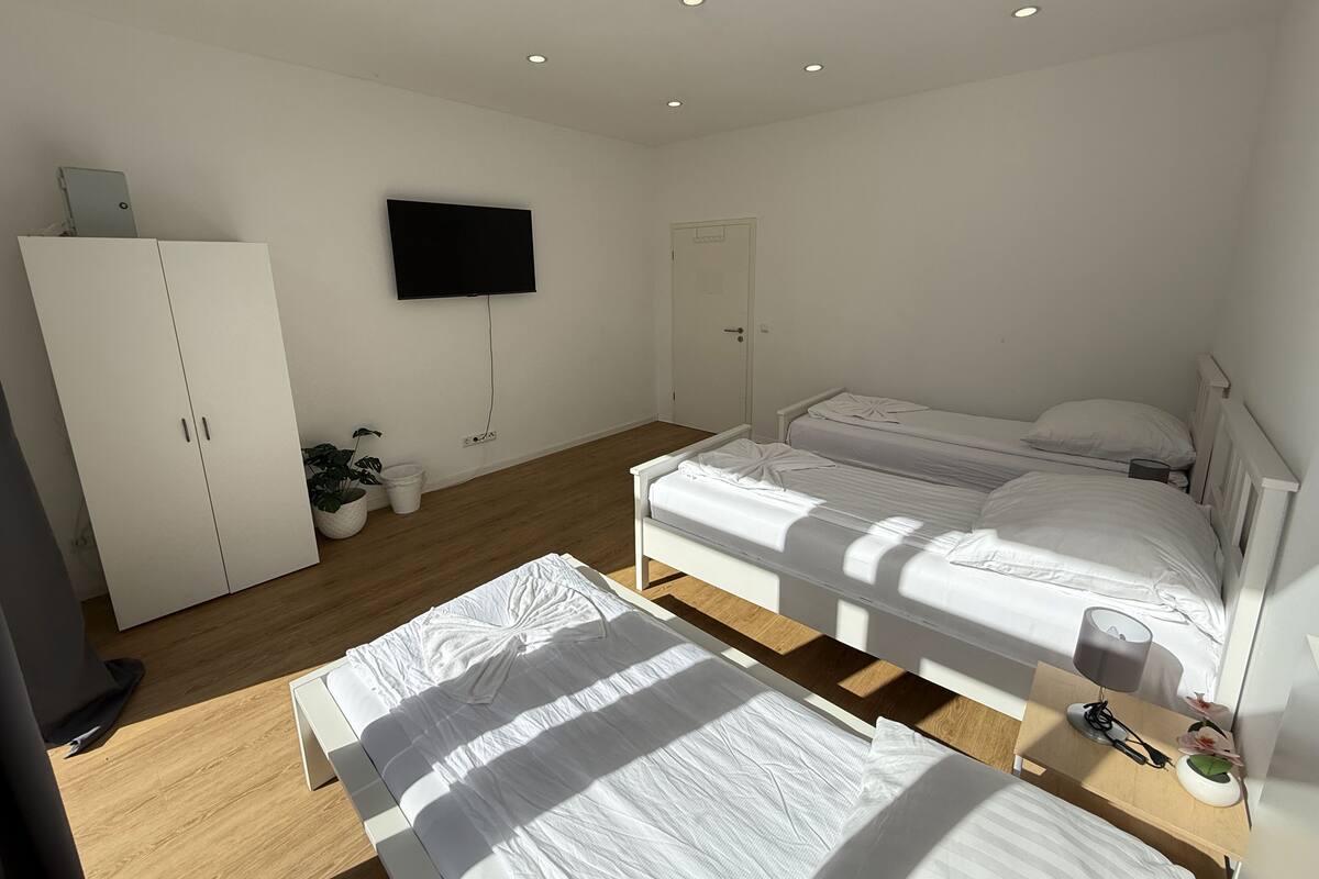 A bedroom with two beds, a wardrobe, a television, and a door.