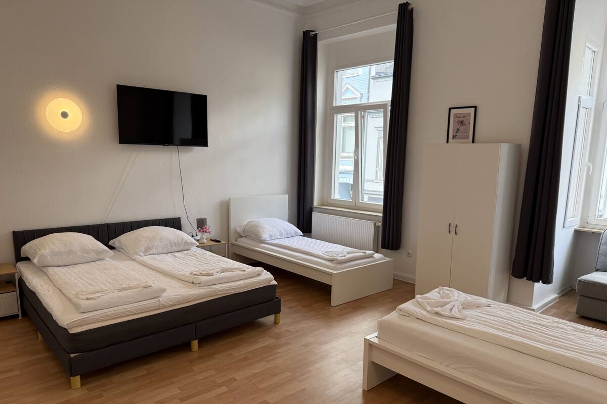 A hotel room with a bed, a TV, a window with curtains, a radiator, and a wardrobe.
