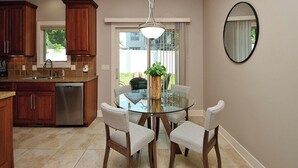 A modern kitchen with a glass dining table, wooden cabinets, and a stainless steel dishwasher. - 4 miles to " The Chuck" for CWS, 3 bed each with private bath, super clean! (Omaha)