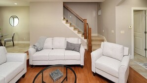 A living room with a staircase, two white sofas, a coffee table, and a mirror. - 4 miles to " The Chuck" for CWS, 3 bed each with private bath, super clean! (Omaha)