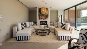 A modern living room with a sectional sofa, a round coffee table, and a large painting above the fireplace. - Exclusive villa with 5 suites, heated pool and panoramic view (Marrakech)