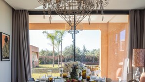 A dining area with a table set for a meal, a chandelier, and a view of the outdoors. - Exclusive villa with 5 suites, heated pool and panoramic view (Marrakech)