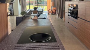 A modern kitchen with a central island, a dining area with a chandelier, and a view of the outdoors. - Exclusive villa with 5 suites, heated pool and panoramic view (Marrakech)