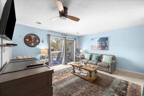 A living room with a sofa, coffee table, and a TV. There is a clock on the wall and a ceiling fan. - Cozy 1-bedroom condo ,2 minute walk to beach! (Myrtle Beach)