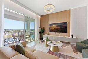 A modern living room with a large TV, a balcony with outdoor furniture, and a city view. - Storey Lake 6 guests brand new lake & club view (Kissimmee)