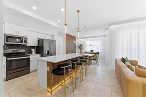 A modern kitchen with white cabinets, stainless steel appliances, and a central island with bar stools. - Storey Lake 6 guests brand new club & lake view (Kissimmee)
