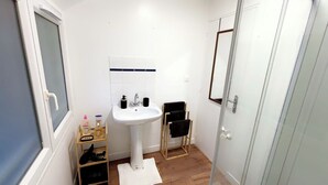 A small bathroom with a white sink, a mirror, and a wooden shelf with toiletries.