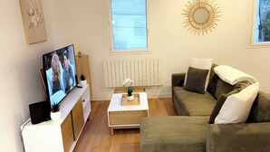 A living room with a television, a wooden coffee table, a green sofa, and a decorative sun-like wall piece.