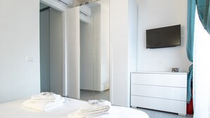 Moderni hotellihuone, jossa on sänky, lipasto, televisio ja peili.