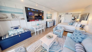 A modern living room with a flat-screen TV, seating area, and a kitchen in the background.