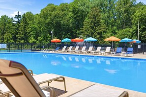 Une piscine entourée d’une clôture et d’arbres, avec des chaises longues et des parasols.