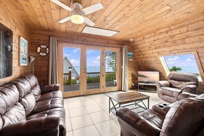 A cabin with a wooden interior, a ceiling fan, a sofa, a recliner, a coffee table, and a TV. - Juniper Presents Chalet #36 The Perfect View: Lake View & Resort Amenities (Stevensville)