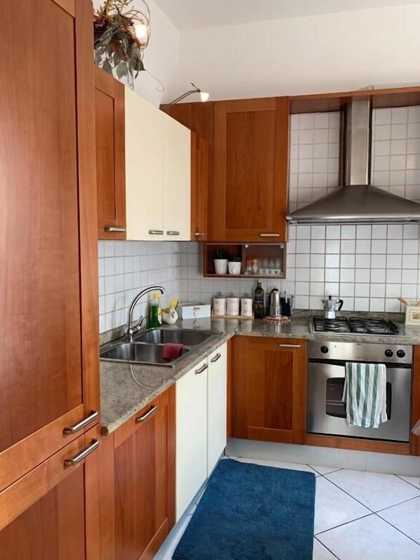 A kitchen with wooden cabinets, a stainless steel stove, and a tiled backsplash. - App. Accanto ai Mercatini di Natale (Trento)