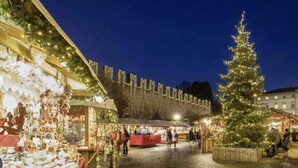 A market square with stalls, a Christmas tree, and a building with illuminated windows. - App. Accanto ai Mercatini di Natale (Trento)