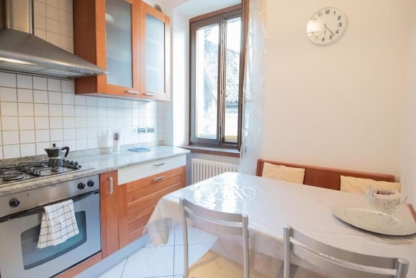 Una cocina con estufa, horno y ventana. Hay una mesa con sillas y un reloj en la pared.