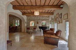 Un ambiente spazioso con parete in pietra, travi in legno a vista, un pianoforte, poltrone in pelle e quadri appesi alle pareti.