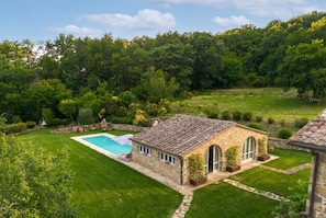 Una casa in pietra con piscina, immersa nel verde e circondata da un paesaggio collinare.