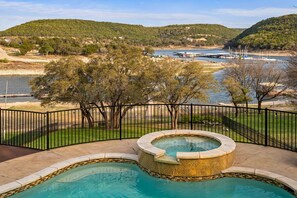 Una piscina con un jacuzzi, rodeada por una valla, con vistas a un río y colinas al fondo.